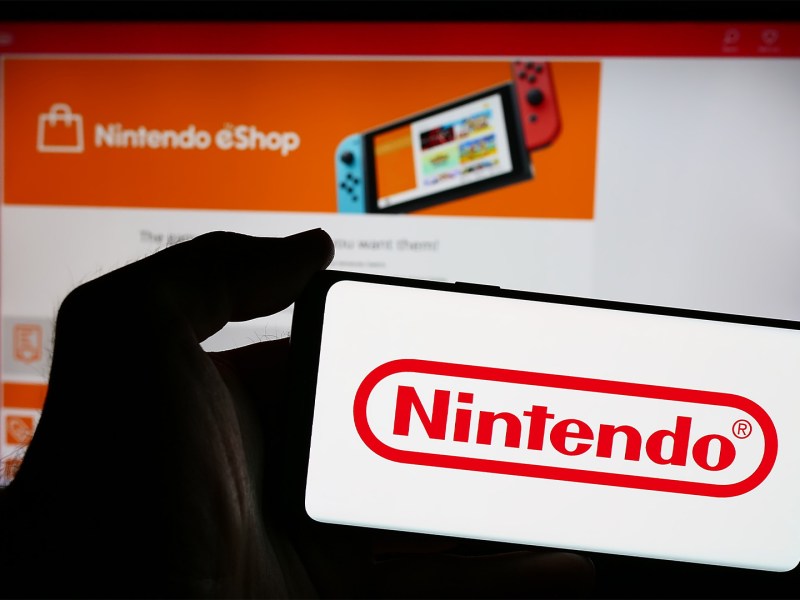 Smartphone mit dem Nintendo-Logo vor einem Bildschirm, auf dem der Nintendo eShop geöffnet ist.